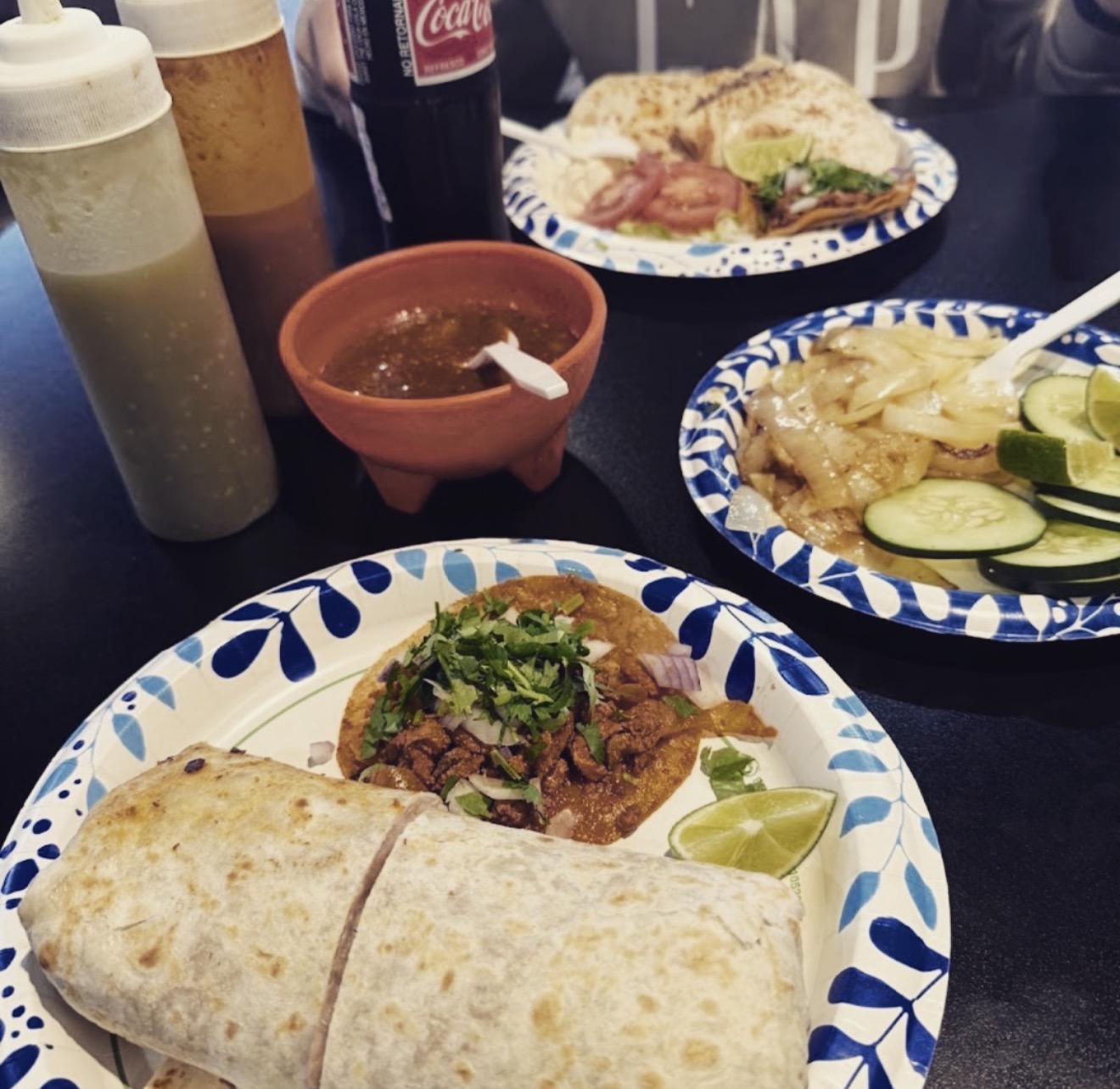 Taqueria table with salsas, cucumber salad, a taco and a burrito